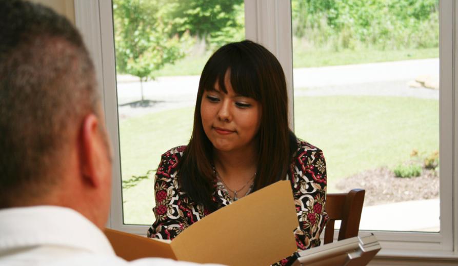 A person with long dark hair reading from a file.