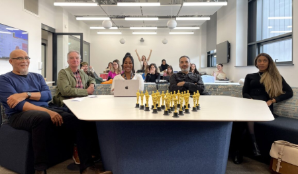 Students and staff sitting on a table surrounding some award trophies