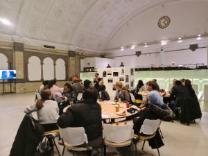 Students and researchers listening to presentation sitting on round tables