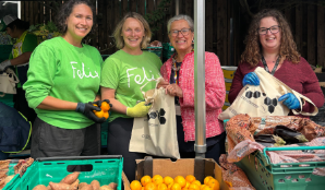 4 people standing in behind a selection of fruit and veg with cotton tote bags