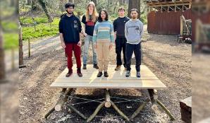 Five students stand on top of a wooden deck in a woodland clearing